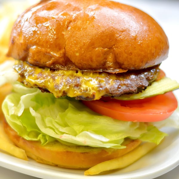 Close-up of a cheeseburger with lettuce, tomato, and pickles on a white plate.