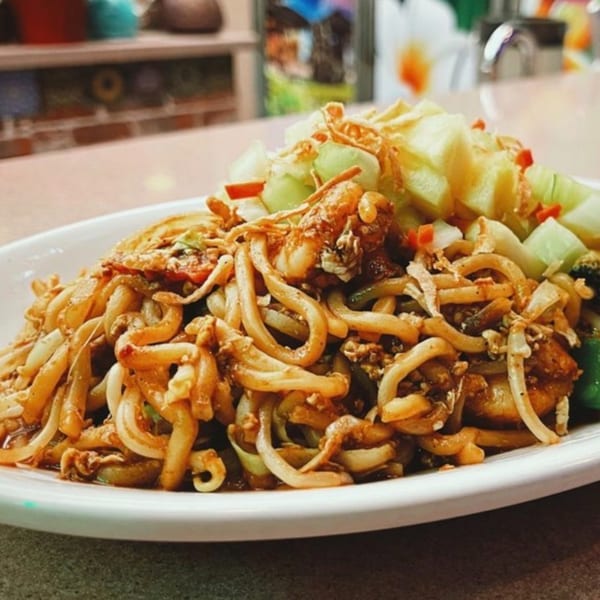 Indonesian stir-fried noodles with chicken, vegetables, and crispy fried shallots on a white plate.