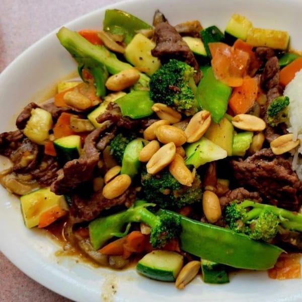 Indonesian beef stir-fry with broccoli, zucchini, carrots, and peanuts, served with white rice.