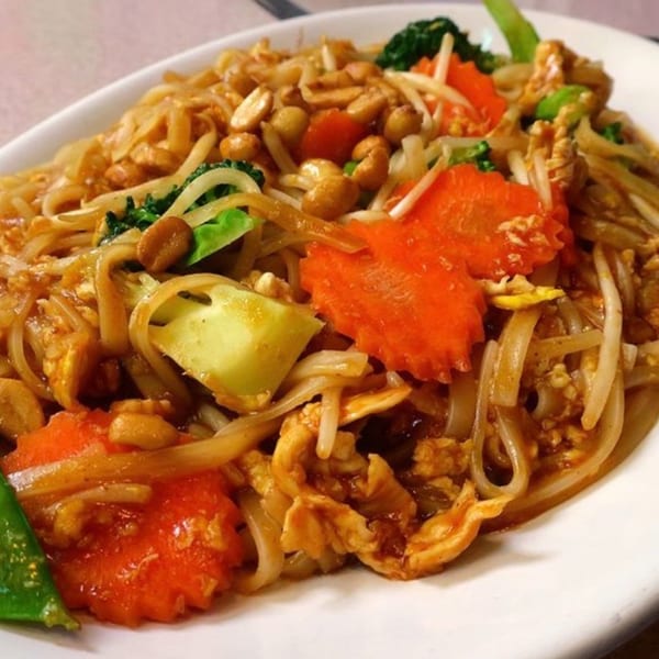 Indonesian stir-fried noodles with chicken, peanuts, broccoli, carrots, and bean sprouts on a white plate.