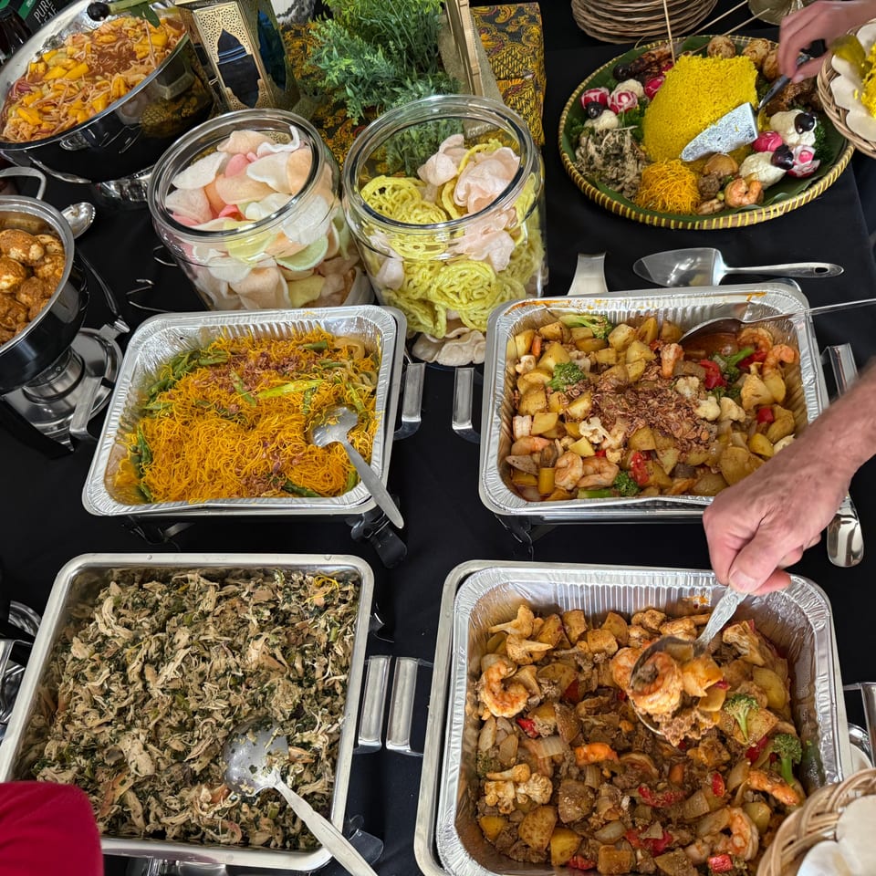 A buffet spread of Indonesian dishes, including yellow rice, noodles, shrimp, and chicken.