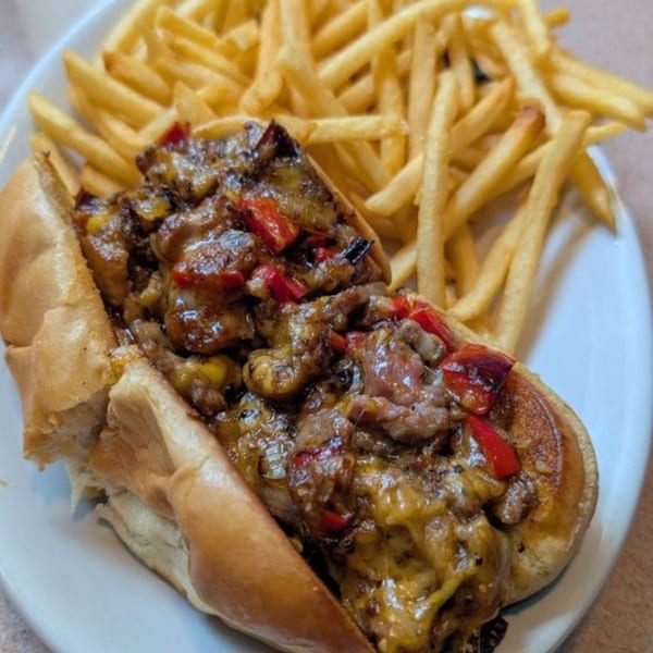 Cheesesteak sandwich with red peppers and melted cheese, served with a side of golden french fries.