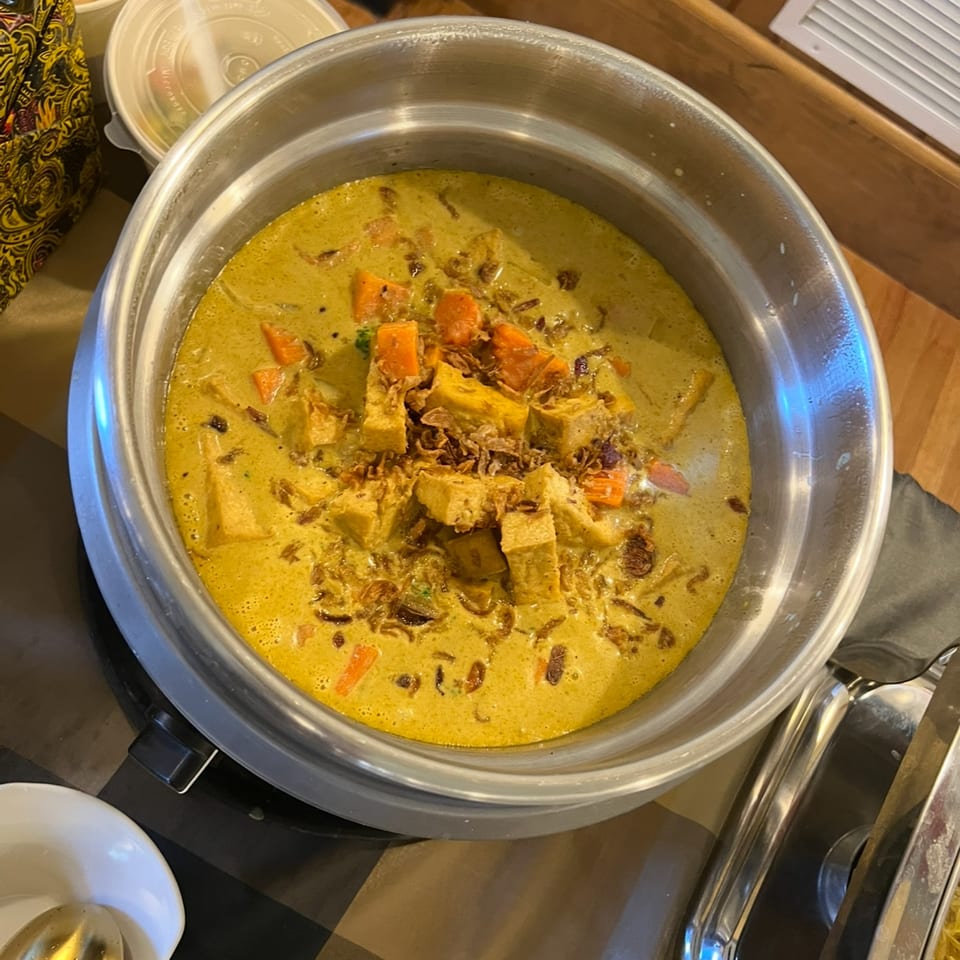 A large metal pot filled with Indonesian curry, tofu, carrots, and fried shallots.