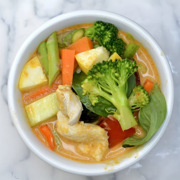 Overhead view of an Indonesian curry with chicken, broccoli, carrots, and other vegetables in a white bowl.