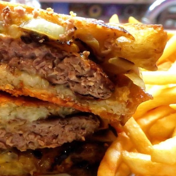 Close-up of a burger with melted cheese and two patties, served with golden french fries.