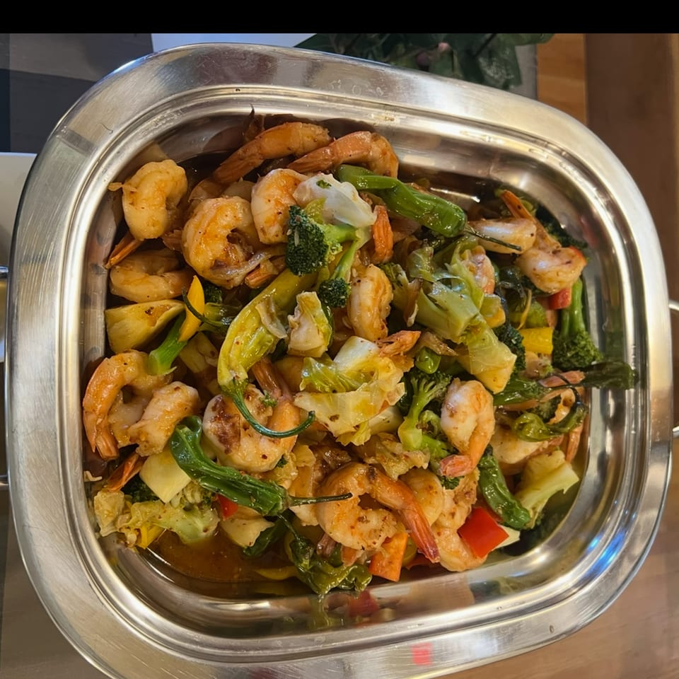 Shrimp stir-fry with broccoli, peppers, and other vegetables in a silver serving dish.